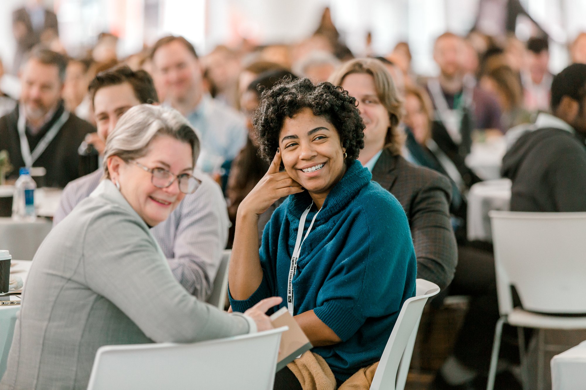 Two women smiling within a large group at a conference Two women smiling within a large group at a conference